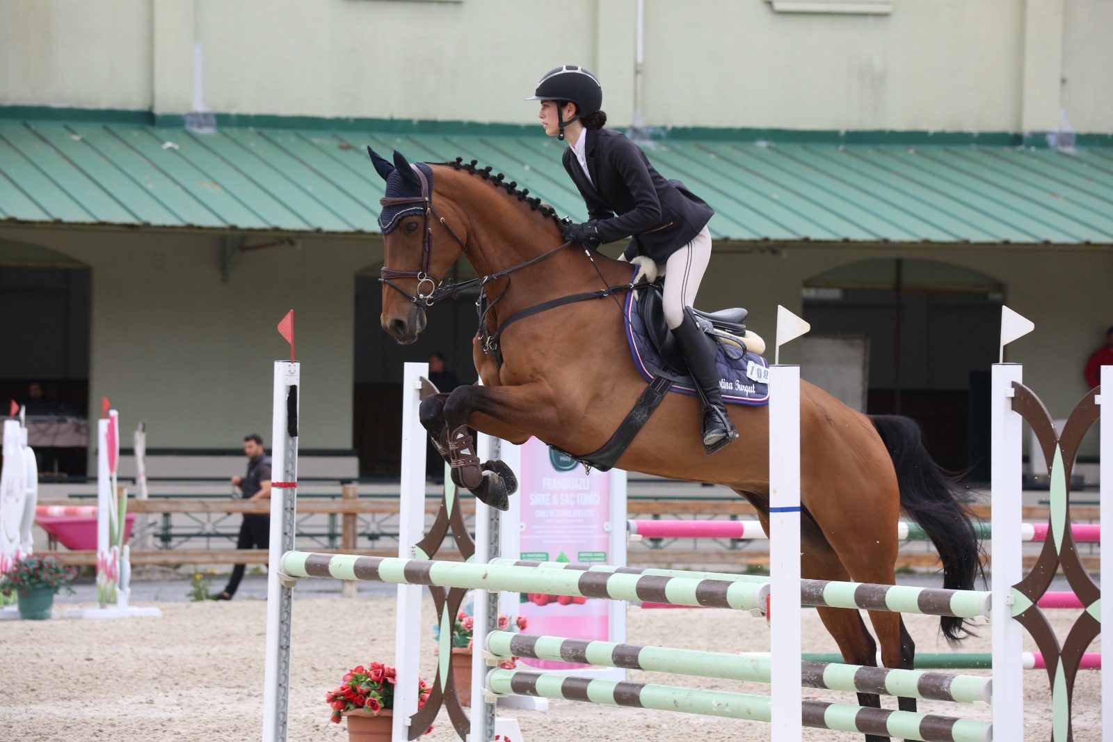 A rider and a bay horse mid-jump over a fence at a show jumping competition